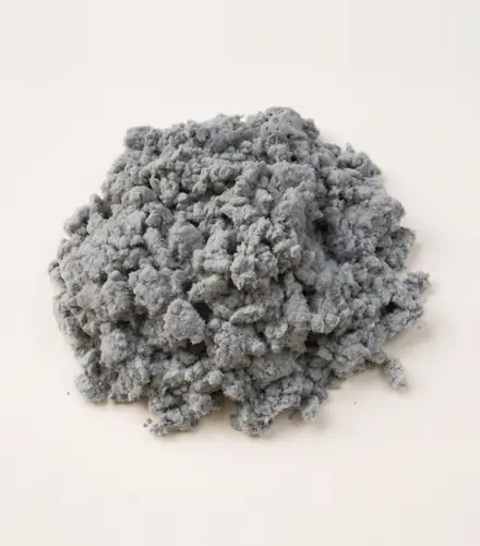 A loose heap of grey FC series cellulose fibre in soft, fibrous crumbs on off-white paper