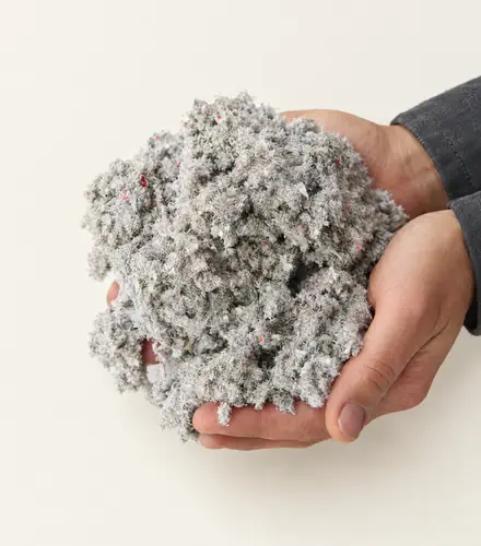 Two hands holding a loose handful of grey cellulose insulation flecked with coloured paper