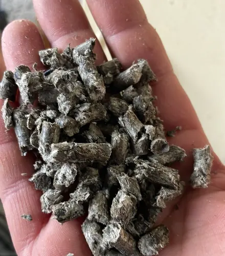 A handful of grey HLB-FIBER pellets held in an open palm