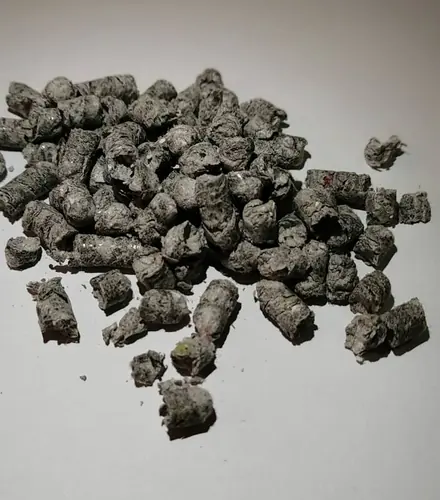 Loose grey HLB-FIBER pellets scattered on a white surface