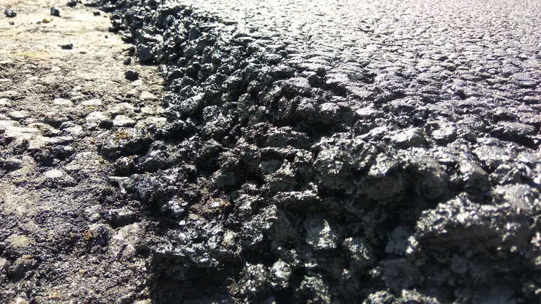 The edge of a freshly laid stone mastic asphalt course: coarse stone bound in glossy black mastic, against the bare base beside it